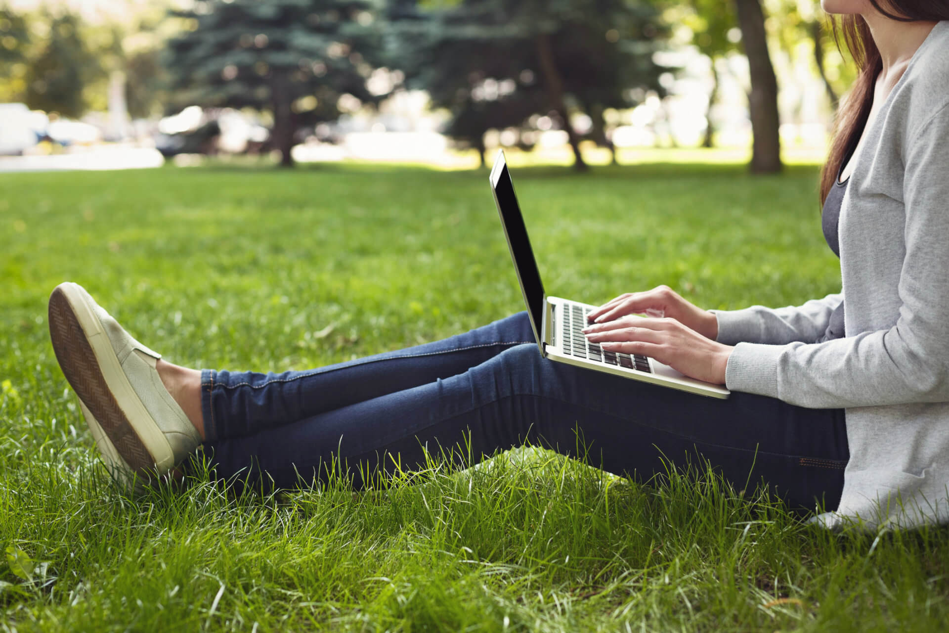 woman sitting on grass typing on a laptop
