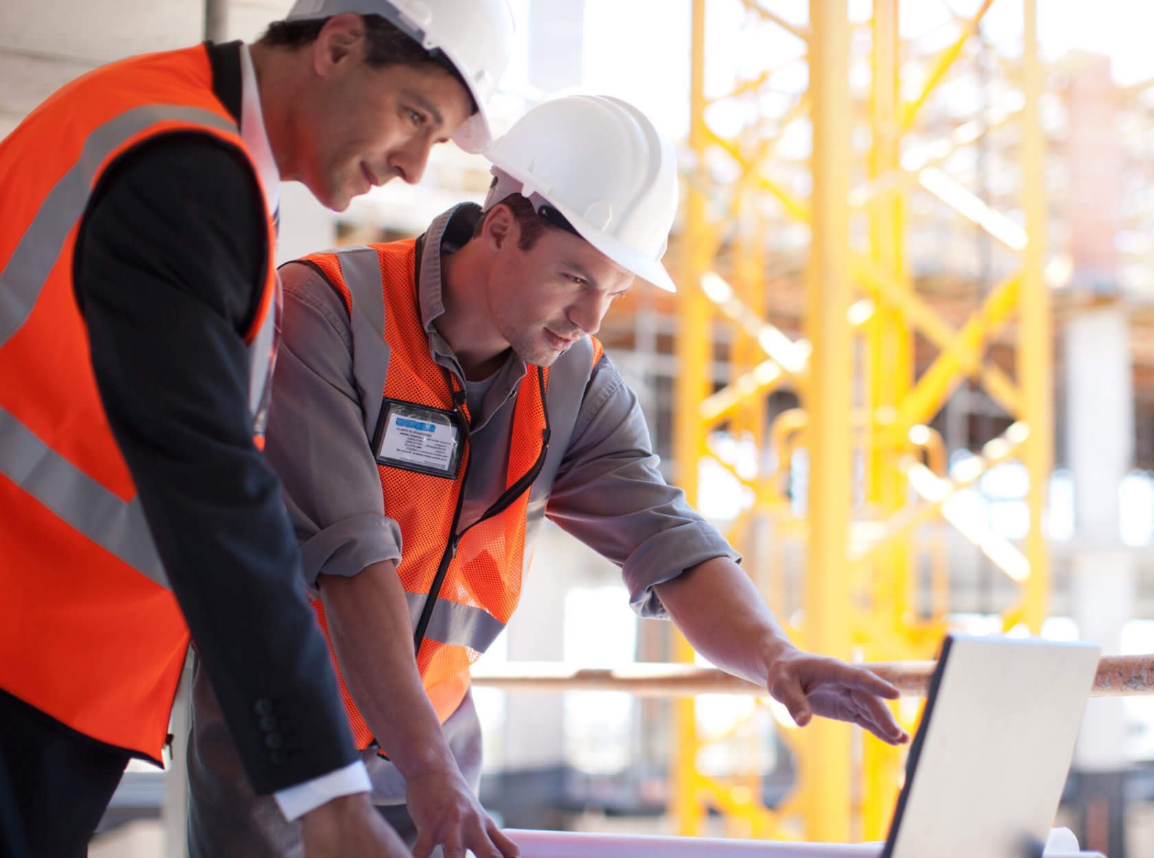 two construction workers looking at a laptop on a construction site
