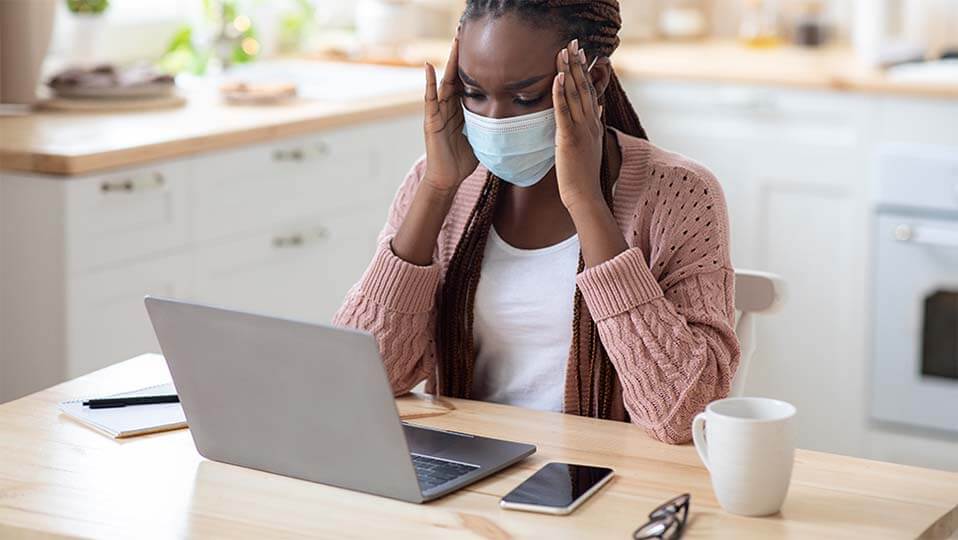 Stressed person in medial mask suffering problems while working on laptop