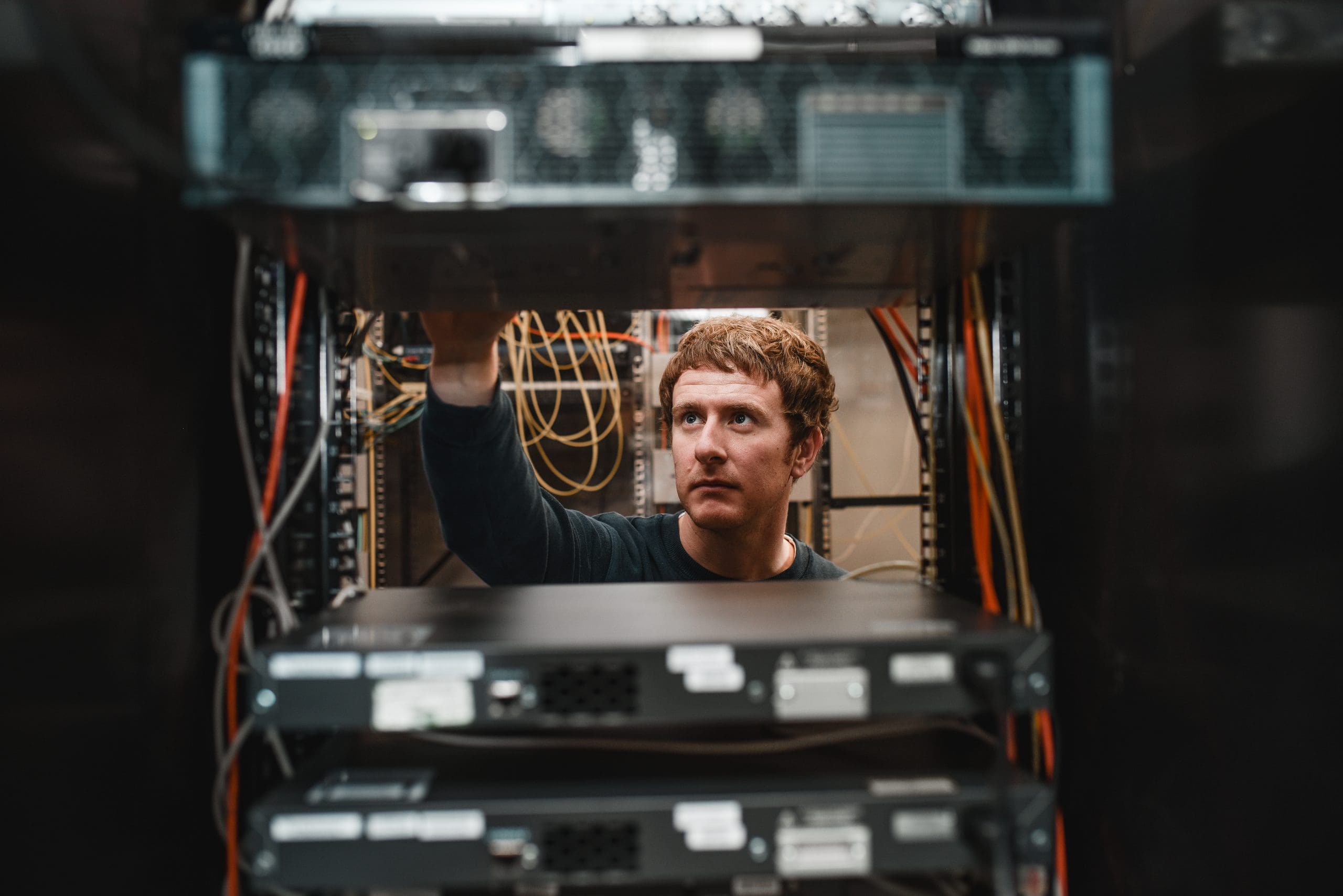 Photograph taken of Cantium employee through a server rack while they are performing maintenance and routine checks.