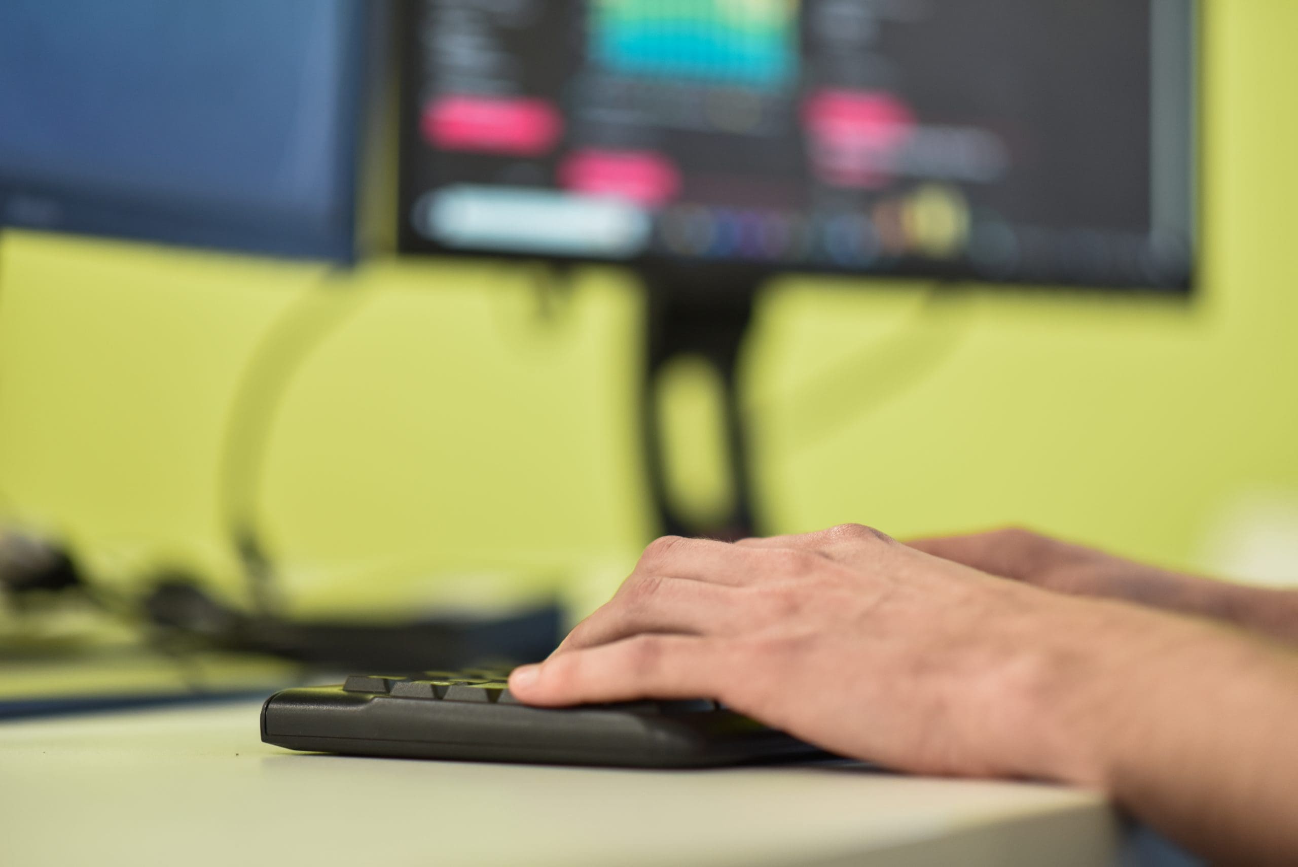 Photograph of two hands typing on keyboard, infront of two desktop monitors, one showing an analytics dashboard.