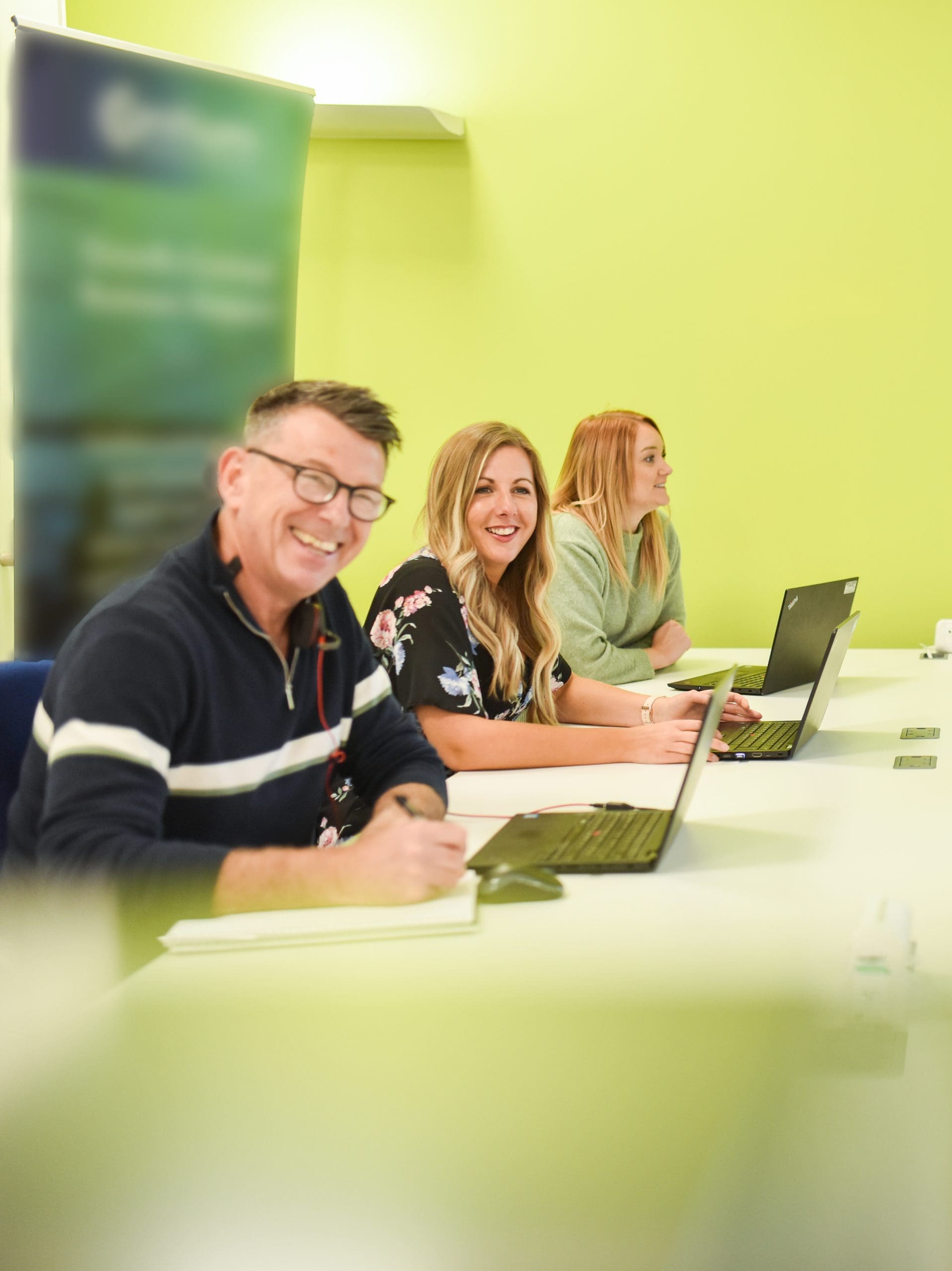 Photograph of 3 Cantium employees having a meeting with laptops while smiling off camera.