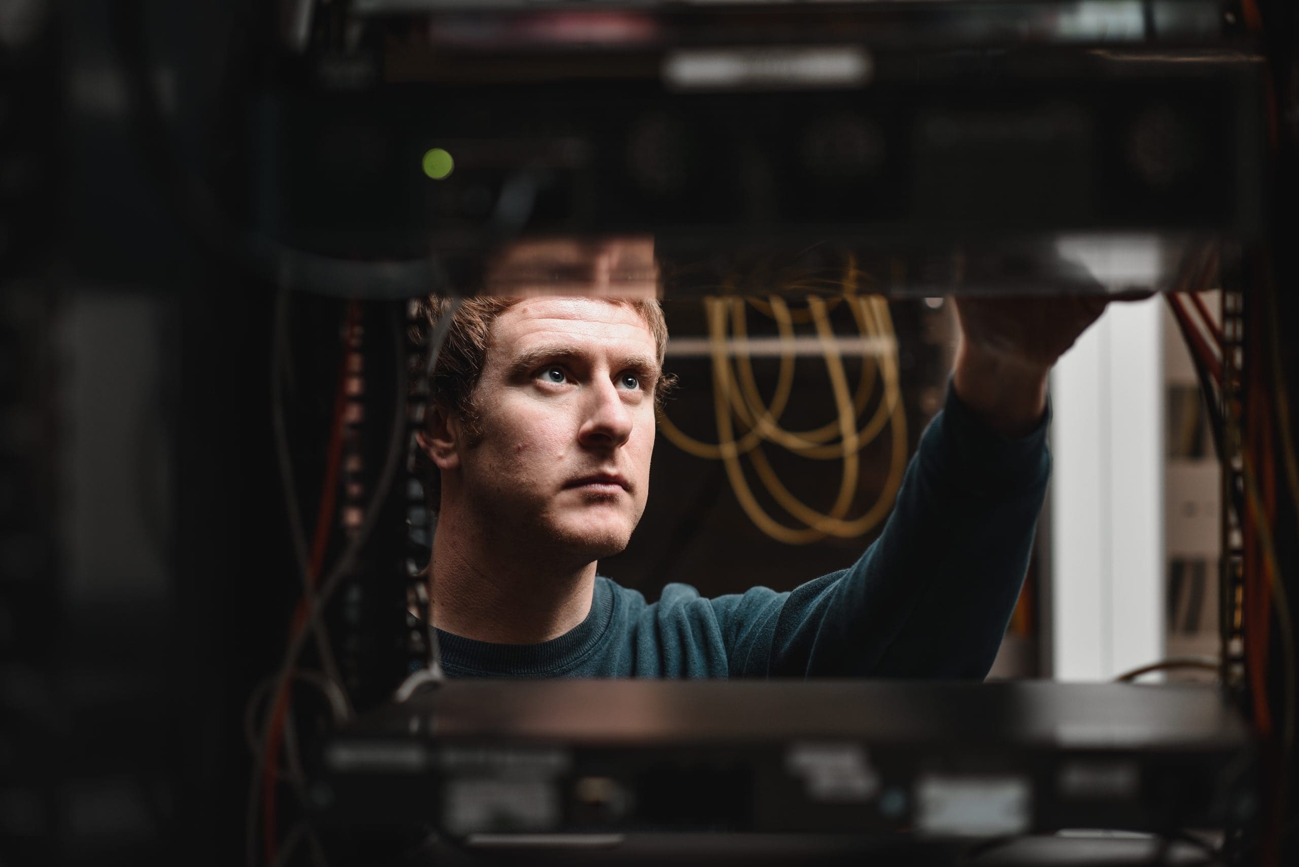 Photograph taken of Cantium employee through a server rack while they are performing maintenance and routine checks.
