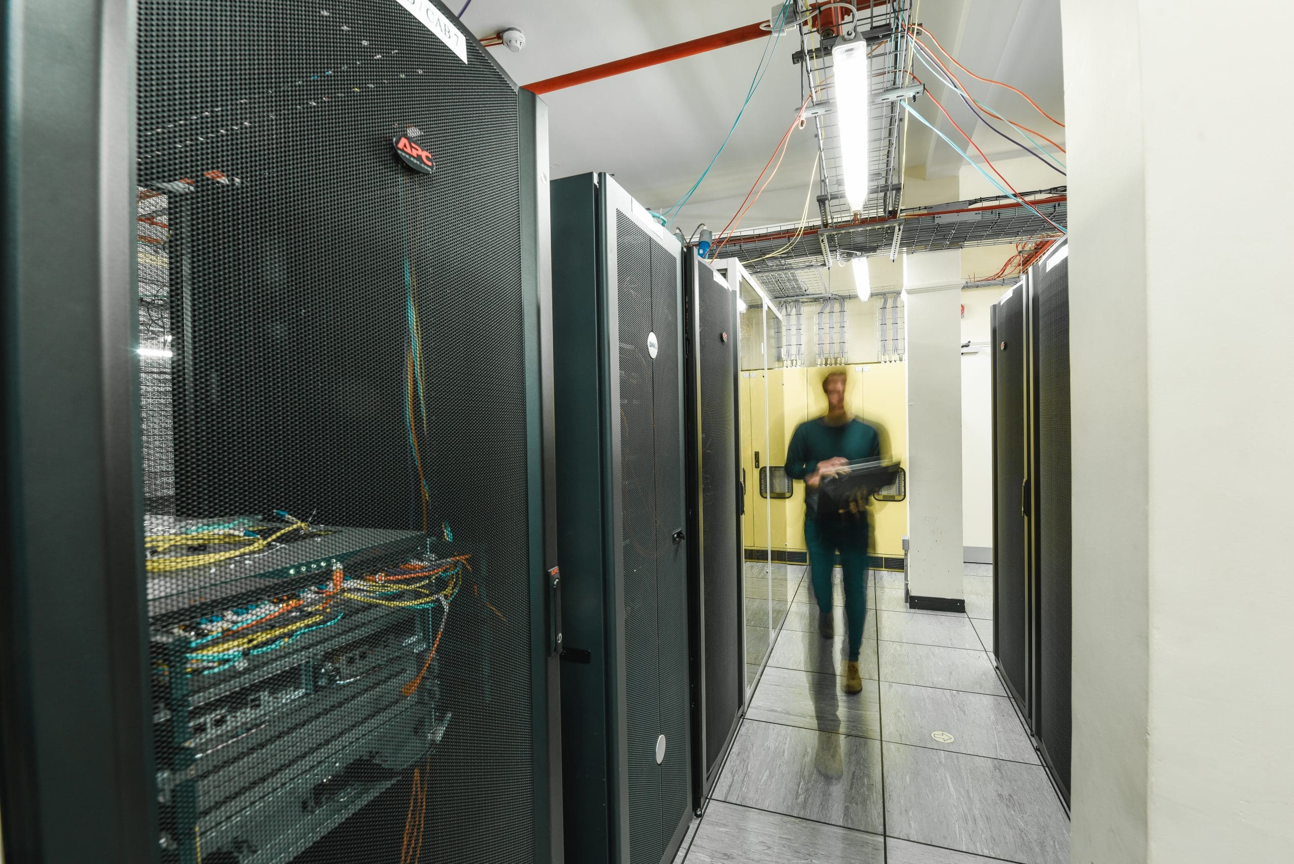 Photograph of a blurred person walking through a data centre.