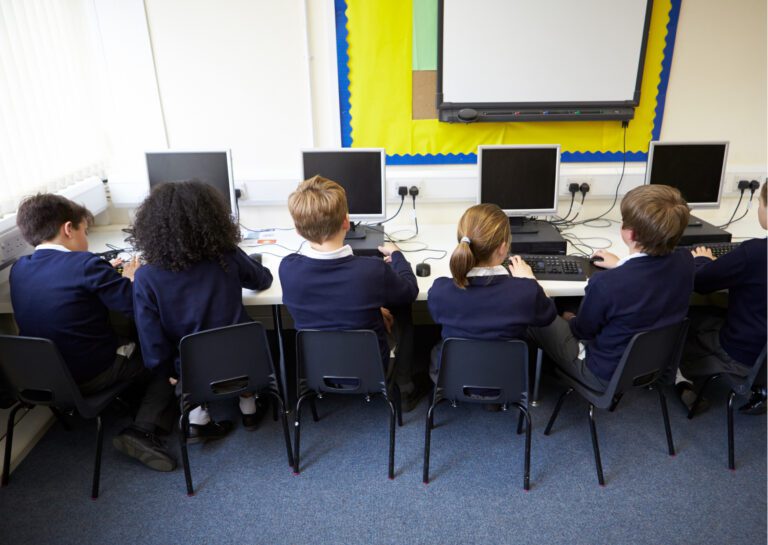 5 school children sitting at computers in school uniform