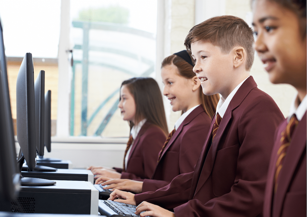 four school children in uniform sitting at and typing on computers