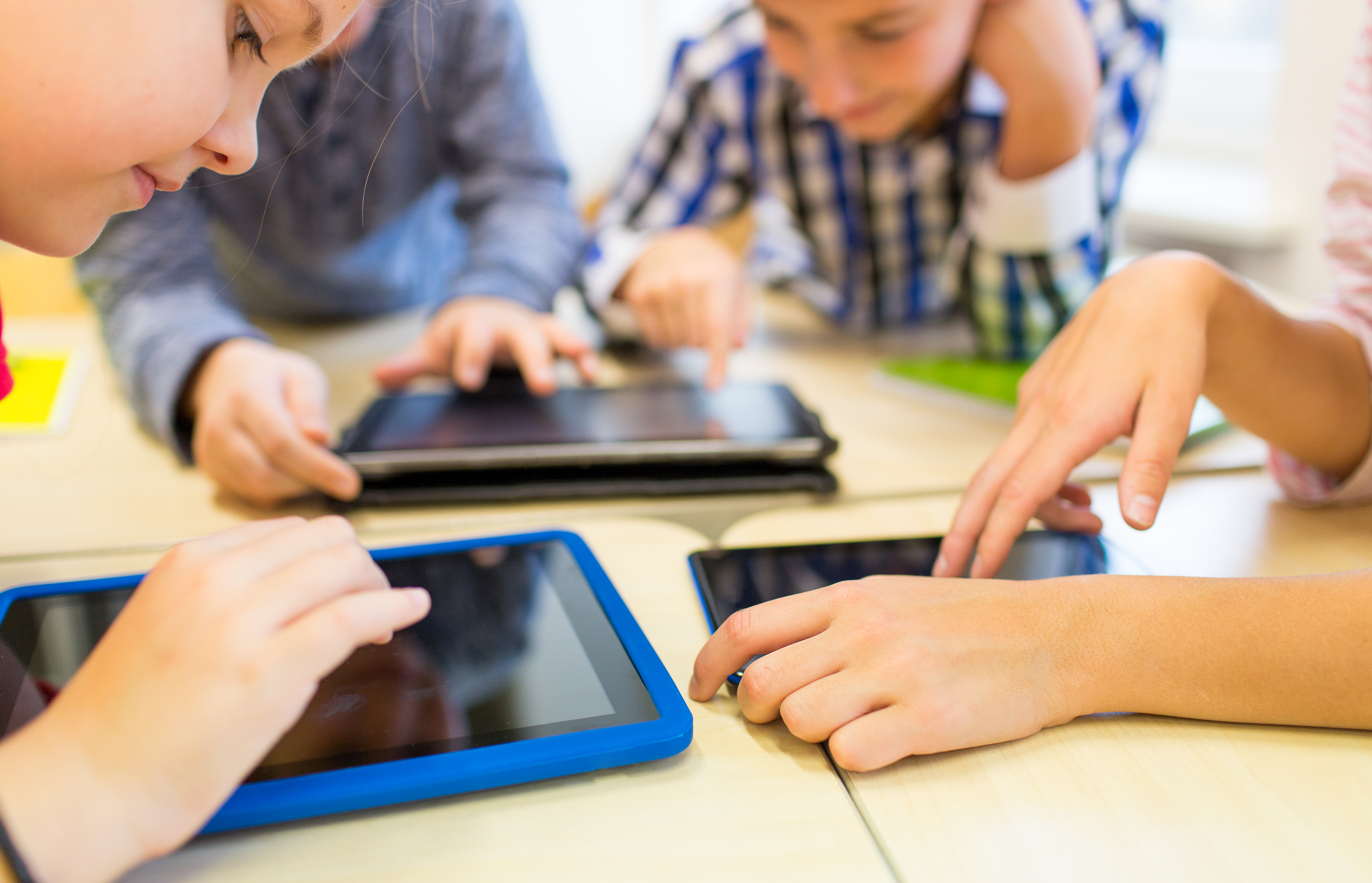 four young people typing on tablets on a desk