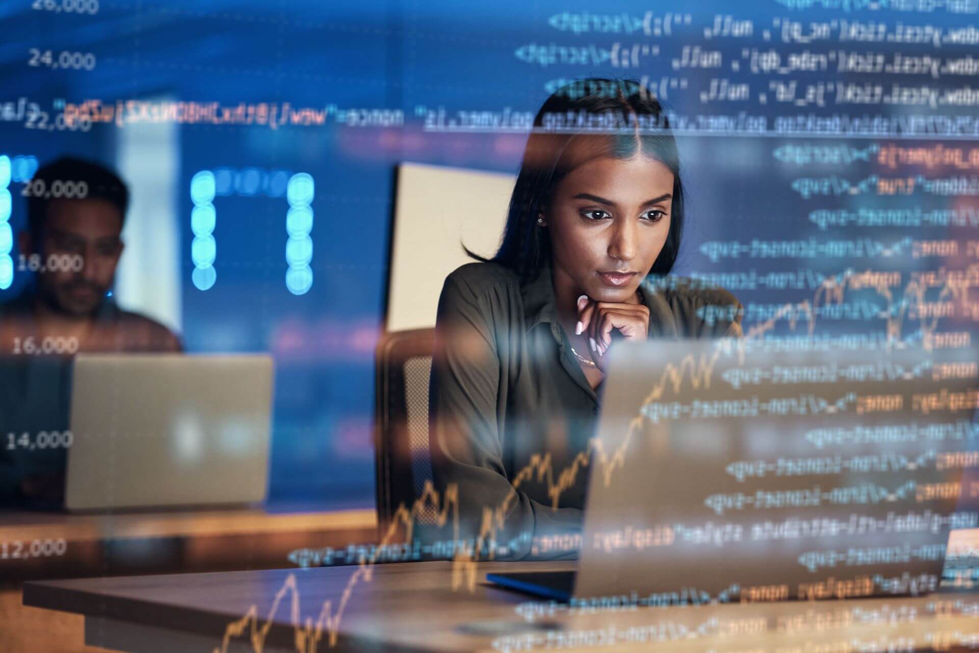 Woman sitting in front of laptop, planning IT transition, with code hologram overlay